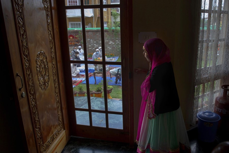 A Kashmiri girl watches from inside her house as men offer Eid prayers in the premises of a residential building in Srinagar.